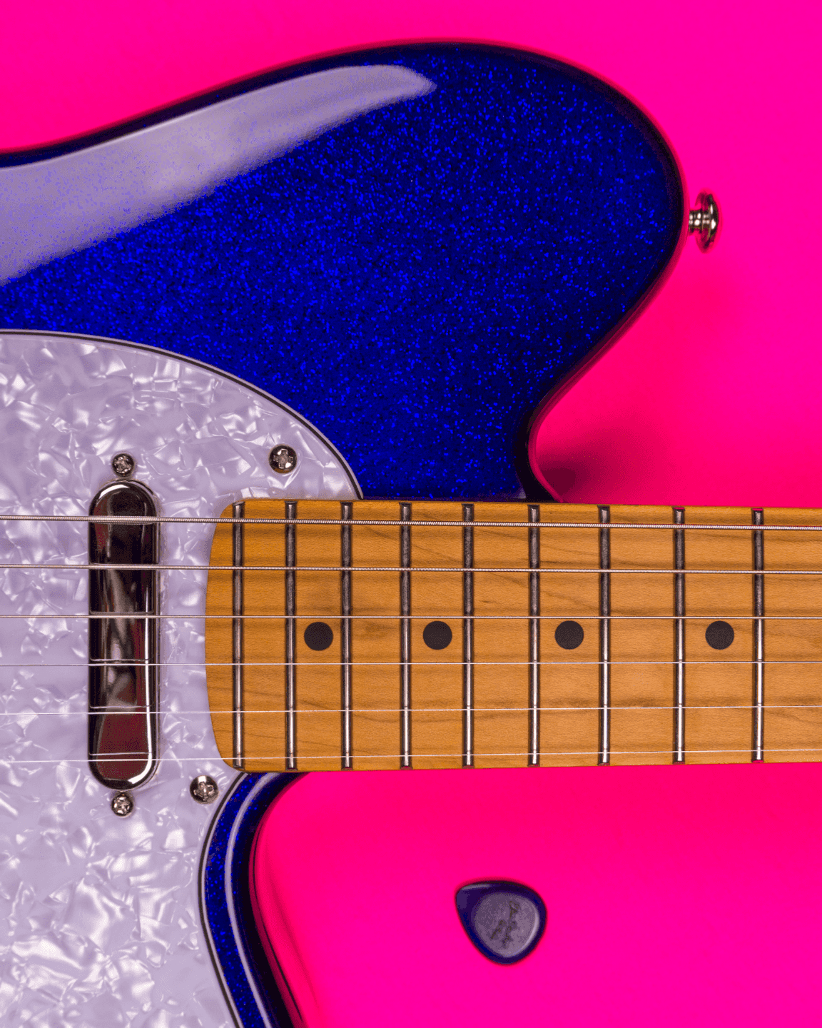 Ultra close view of a Talman TM302PM-BSP (blue sparkle) with a purple Dunlop guitar pick, both resting on a pink background